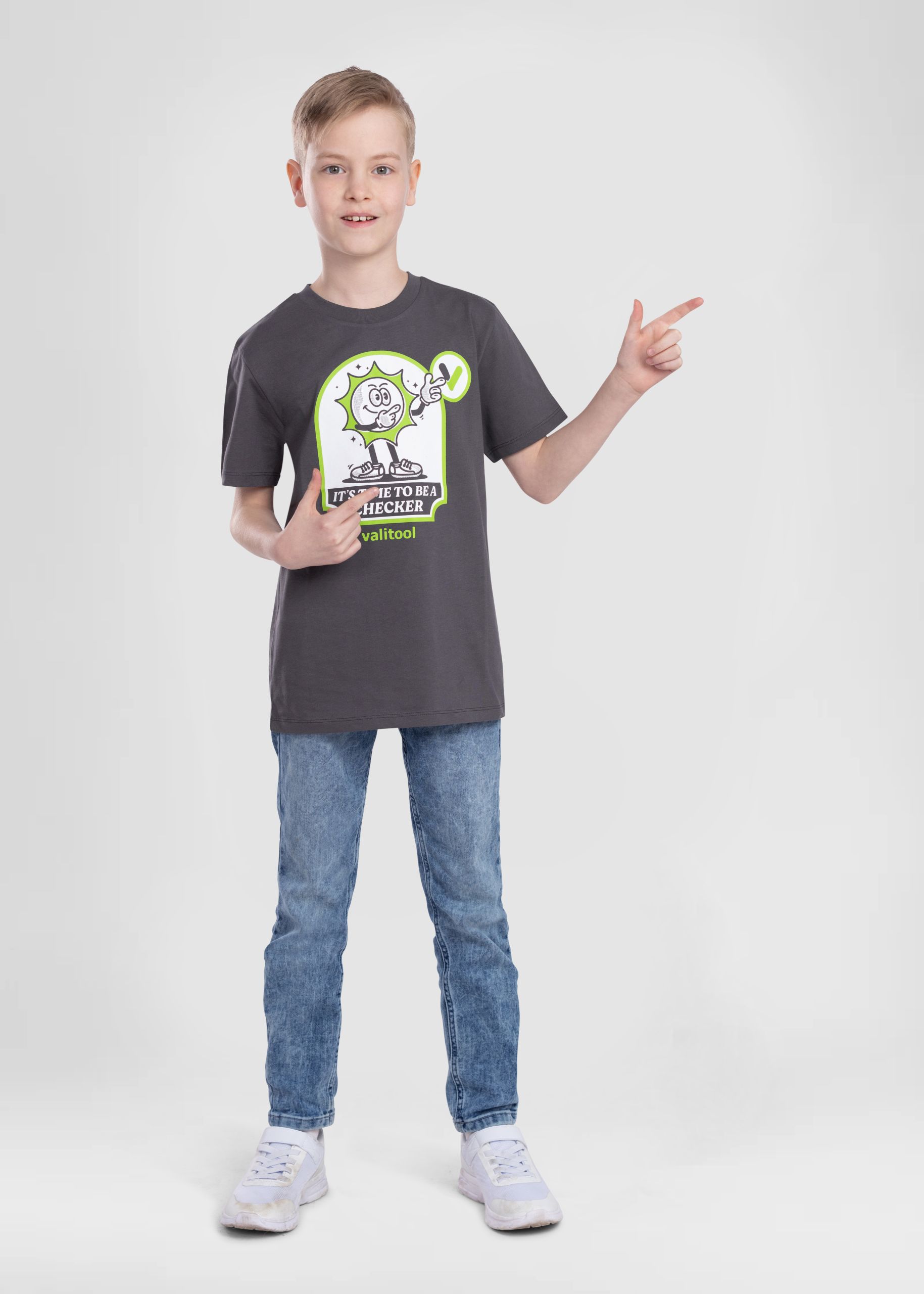 Junge trägt Valitool Kinder Unisex T-Shirt in Anthrazit mit Cartoon-Print ‚It’s Time to Be a Checker‘ und imitiert die Comic-Figur durch dieselbe Geste, Studioaufnahme